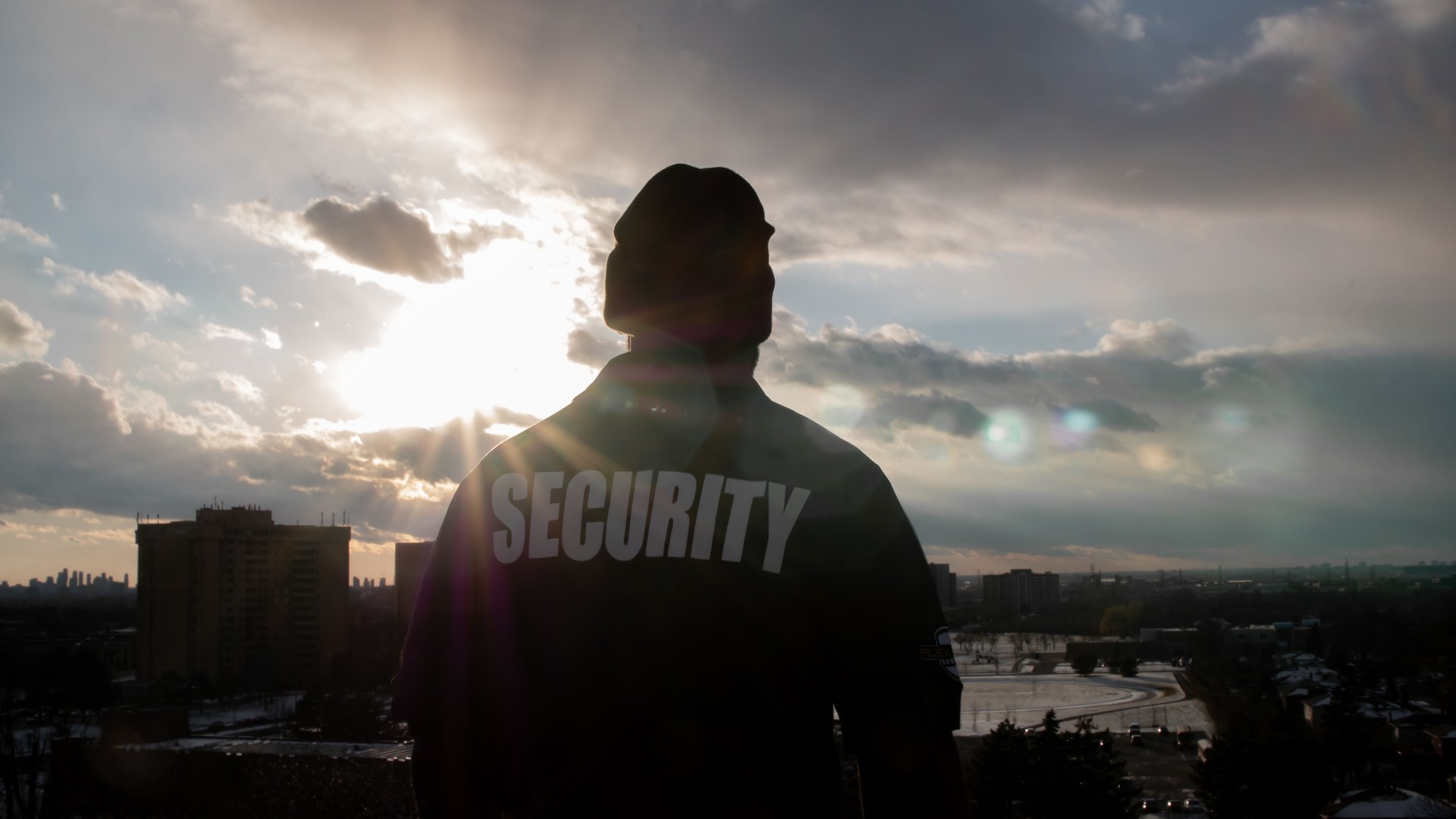 Male security guard in uniform watching over city from the high floor.